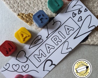 May include: A set of colorful alphabet letter crayons spelling out the name "MARIA" on a white card with a heart design. The crayons are arranged in a line on the card. There is a yellow sticker with the text "CRAYON ALLSORTS" on the card.