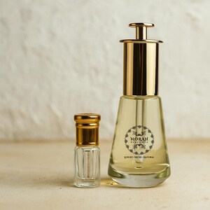 May include: Two perfume bottles. The larger bottle has a gold cap and a clear glass body with a label that reads "NORAH PERFUMES LUXURY - NICHE - NATURAL". The smaller bottle is also clear with a gold cap.