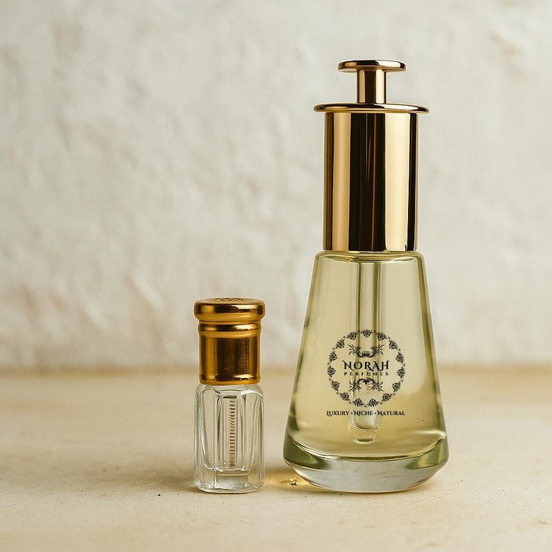 May include: Two perfume bottles. The larger bottle has a gold cap and a clear glass body with a label that reads "NORAH PERFUMES LUXURY - NICHE - NATURAL". The smaller bottle is also clear with a gold cap.
