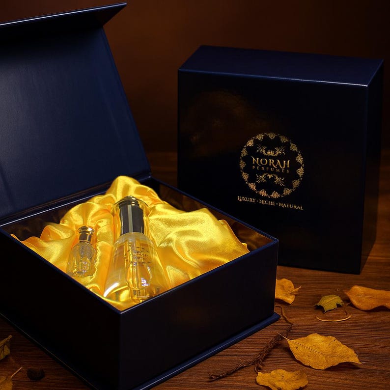 May include: A navy blue gift box with a gold logo and the text "NORAH PERFUMES". Inside, two perfume bottles rest on a bed of yellow satin. The box is open, revealing the bottles and satin. The second box is closed.