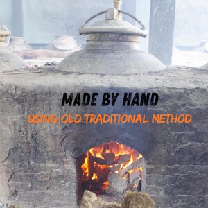 May include: A stone oven with a domed top and a fire burning inside. The text "MADE BY HAND" is above "USING OLD TRADITIONAL METHOD". The image suggests traditional craftsmanship and artisanal production methods.