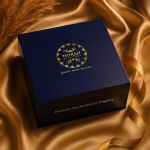 May include: A navy blue box with gold lettering and a gold logo that reads "NORAH PERFUMES". The box has the words "LUXURY - NICHE - NATURAL" and "Embrace the Essence of Elegance" printed on it. The box is on a gold satin surface.