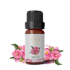 Può includere: Una bottiglia di vetro marrone di olio di rosa con tappo nero, etichettata "NORAH PERFUMES" e "ROSE OIL 0.33 fl. oz / 10ml." La bottiglia è circondata da rose rosa e foglie verdi, con il testo "100% Pure."