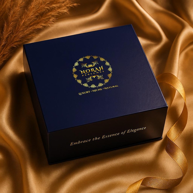 Puede incluir: Una caja azul marino con letras doradas y un logotipo dorado que dice "NORAH PERFUMES". La caja tiene las palabras "LUJO - NICHO - NATURAL" y "Abraza la Esencia de la Elegancia" impresas. La caja est&aacute; sobre una superficie de sat&eacute;n dorado.