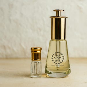May include: Two perfume bottles. The larger bottle has a gold cap and a clear glass body with a label that reads "NORAH PERFUMES LUXURY - NICHE - NATURAL". The smaller bottle is also clear with a gold cap.