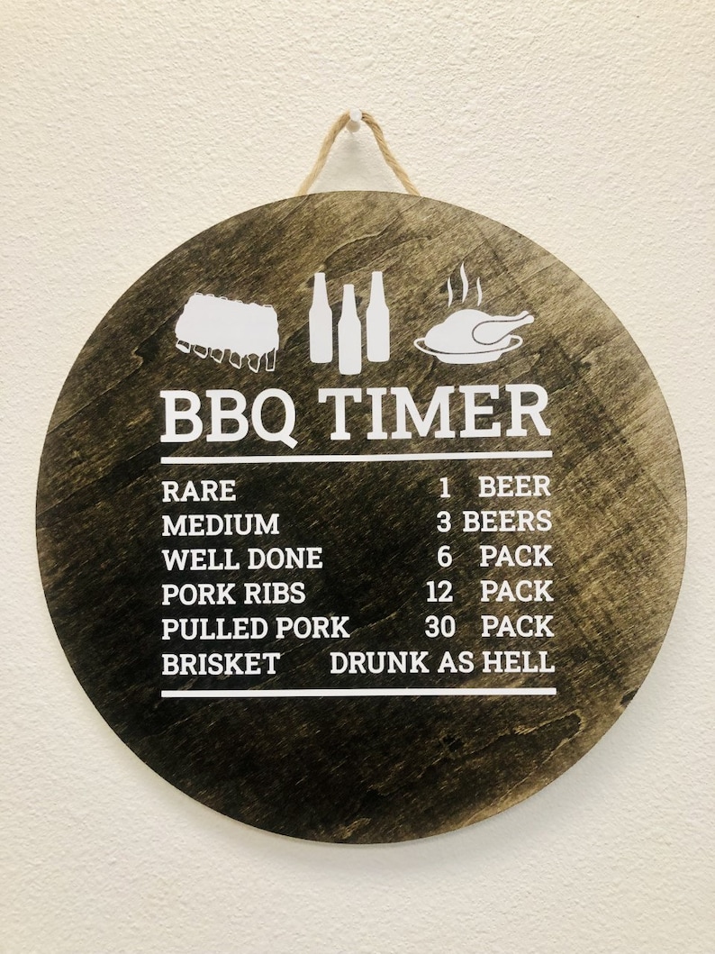 May include: A round wooden sign with a white background and black text that reads "BBQ TIMER". The sign has a list of different types of meat and the corresponding number of beers to drink while cooking them. The list includes: Rare - 1 Beer, Medium - 3 Beers, Well Done - 6 Pack, Pork Ribs - 12 Pack, Pulled Pork - 30 Pack, Brisket - Drunk as Hell.
