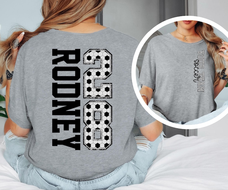 May include: A gray t-shirt with the name "Rodney" and the number "28" in a black, soccer ball-themed design on the back. The word "soccer" is printed vertically on the front of the shirt.