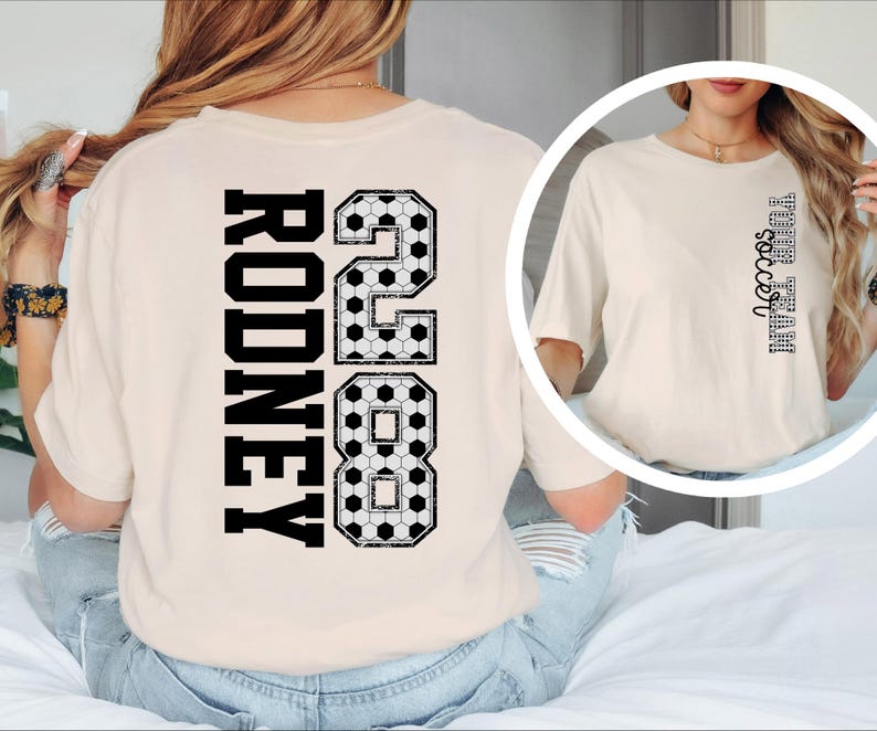 May include: Cream-colored t-shirt with the name "RODNEY" and the number "28" in black, soccer-ball-patterned font on the back. The shirt also features the text "Fall soccer" in a vertical design on the front.