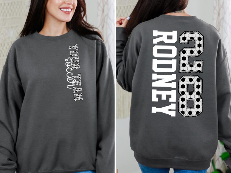 May include: Charcoal gray sweatshirt with the text "YOUR TEAM soccer" vertically on the front. The back features the name "RODNEY" and the number "28" in a soccer ball design. A comfortable, casual top for soccer fans.