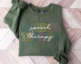May include: A green sweatshirt with the words "speech therapy" printed on the front in rainbow colors.