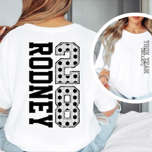 May include: White t-shirt with the name "RODNEY" vertically printed in black block letters, along with the number "28" in a soccer ball design. The shirt also features the text "YOUR TEAM soccer" on the front.