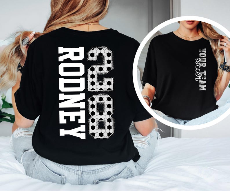 May include: Black t-shirt with the name "RODNEY" and the number "28" in white, soccer ball-themed design. The shirt also features the text "YOUR TEAM soccer" in white. The shirt is a casual style.