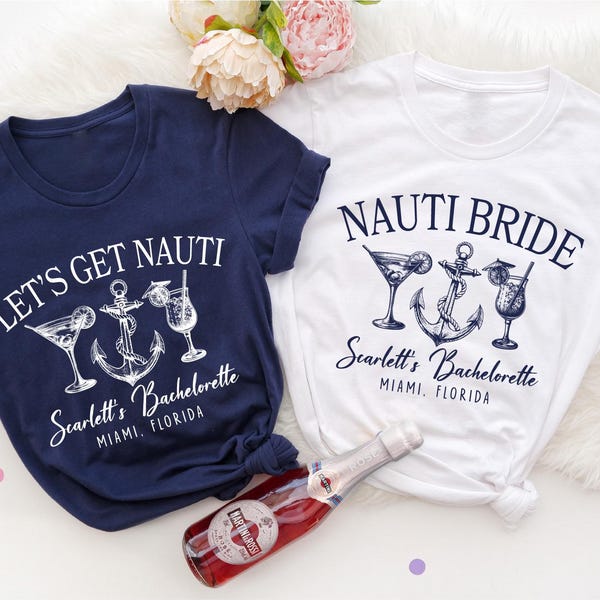 Op de afbeelding: Twee witte T-shirts met een nautisch thema. Eén shirt zegt "Let's Get Nauti" met een anker en cocktailglazen. Het andere shirt zegt "Nauti Bride" met een anker en cocktailglazen. Beide shirts hebben de tekst "Scarlett's Bachelorette Miami, Florida".