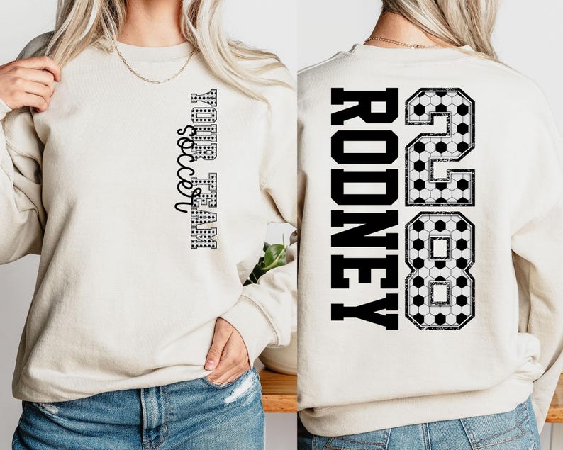 May include: Cream-colored sweatshirt with the text "YOUR TEAM soccer" in black on the front. The back features the name "RODNEY" and the number "28" in black, with a soccer ball pattern.