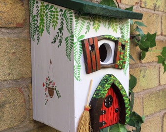 Cadeau d'anniversaire. Cabane à oiseaux peinte à la main dans un style cottage avec une porte de fée rouge, des volets, un balai de fée, un cadeau pour jardiniers, un nichoir