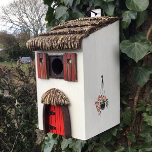 Hand painted white thatched cottage style bird house.  Wooden nesting box with a red thatched door, flower basket, owl and fox , small birds