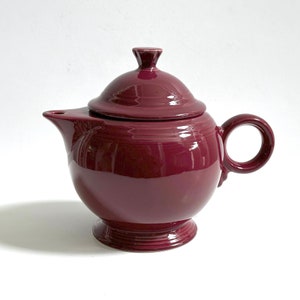 May include: A deep burgundy teapot with a lid and a round body. The teapot has a spout and a handle.