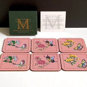 May include: Set of six pink coasters with a floral and butterfly design. The coasters feature a variety of butterflies and flowers in shades of pink, yellow, green, and blue. The coasters are made of cork and have a protective layer to prevent scratches and spills. The coasters are packaged in a box with the Metropolitan Museum of Art logo.