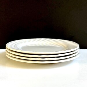 May include: A stack of four white ceramic plates with a wavy design. The plates are stacked on a white surface.