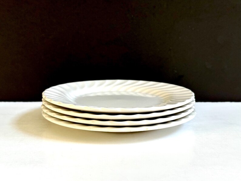 May include: A stack of four white ceramic plates with a wavy design. The plates are stacked on a white surface.