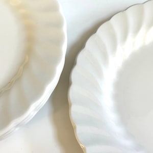 May include: A stack of white ceramic dinner plates with a scalloped edge.