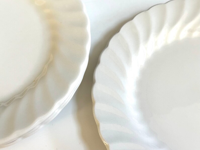 May include: A stack of white ceramic dinner plates with a scalloped edge.