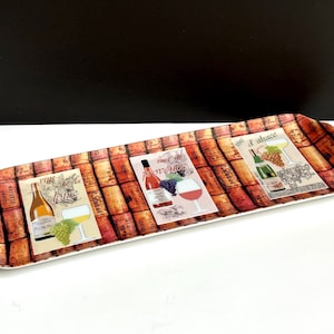 May include: A rectangular serving tray with a cork design and three different wine bottle illustrations. The tray features a white wine bottle with grapes, a red wine bottle with grapes, and a white wine bottle with grapes. The tray is perfect for serving wine and cheese.