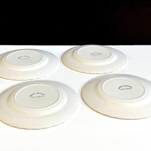 May include: Four white ceramic plates with a scalloped edge. The plates have a raised center and a small inscription on the bottom that reads "Avon Broadsides Made in England".