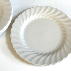 May include: A set of white ceramic dinner plates with a wavy, fluted edge. The plates are stacked on top of each other.