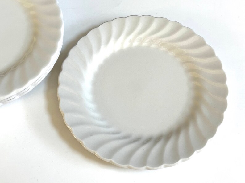 May include: A set of white ceramic dinner plates with a wavy, fluted edge. The plates are stacked on top of each other.