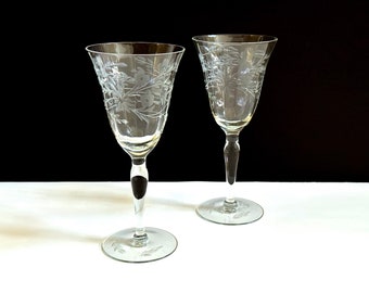 May include: Two clear glass wine glasses with etched floral designs on a white surface.