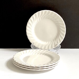 May include: A set of four white ceramic plates with a swirl design. The plates are stacked on top of each other.