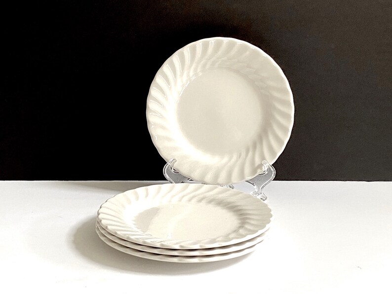 May include: A set of four white ceramic plates with a swirl design. The plates are stacked on top of each other.