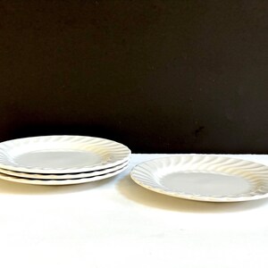 May include: A set of four white ceramic plates with a wavy design. The plates are stacked on top of each other.