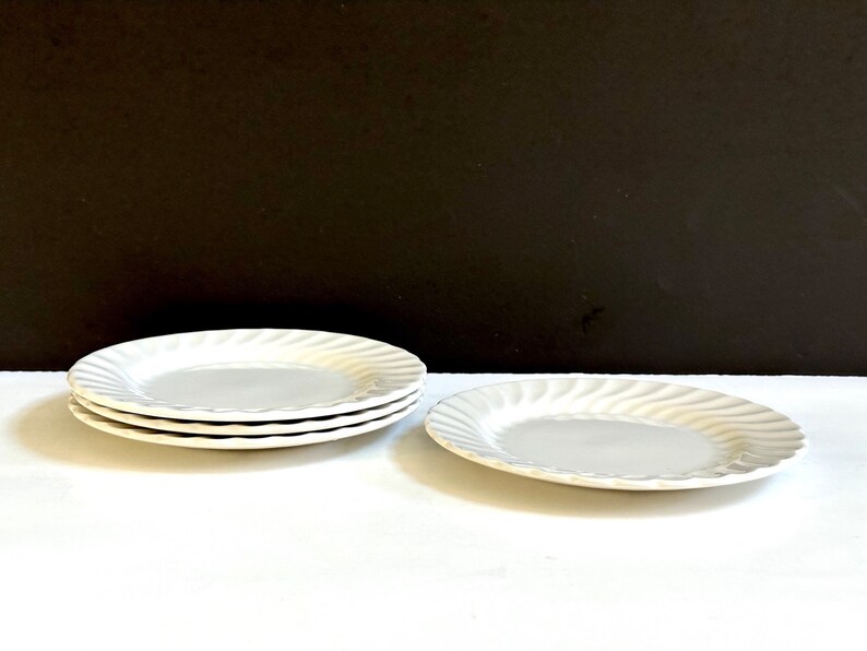 May include: A set of four white ceramic plates with a wavy design. The plates are stacked on top of each other.