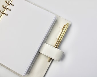 May include: A white leather bound planner with a gold pen tucked into the pen holder. The planner has a ring binder and clear dividers.