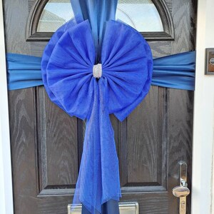 May include: A royal blue bow with a sparkly centre is tied around a dark wood door with a blue satin ribbon.