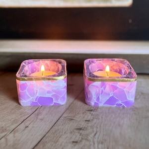 May include: Two purple glass candle holders with gold trim and a lit tea light candle in each.