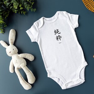 May include: A white baby onesie with short sleeves and poppers at the bottom. The onesie features the Chinese characters for "pure" printed on the front, with the English word "Pure" underneath.