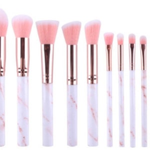 May include: Set of 10 makeup brushes with white handles and pink marble accents. The brushes have soft, pink bristles and gold metal ferrules.