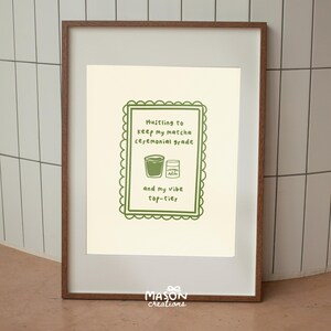 May include: A framed print with a green border and text that reads "Hustling to keep my matcha ceremonial grade and my vibe top-tier". The print features a green illustration of a cup of matcha and a jar of matcha powder.