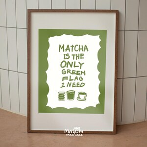 May include: A framed print with a green background and white text that reads "Matcha is the only green flag I need". The text is surrounded by a white cloud shape. There are three green, white, and brown illustrations of matcha tea cups at the bottom of the print.