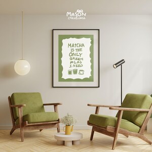 May include: A green and white poster with the text "Matcha is the only green flag I need" and three illustrations of cups of matcha. The poster is hanging on a white wall in a living room with two green armchairs and a small table with a vase of white flowers.