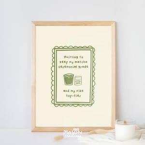 May include: A framed print with a green border and text that reads "Hustling to keep my matcha ceremonial grade and my vibe top-tier". The print features a green illustration of a cup of matcha and a container of matcha powder.