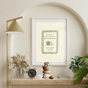 May include: A framed print with a light green background and a white border. The print features a green illustration of a cup of matcha and a matcha powder container. The text reads "Hustling to keep my matcha ceremonial grade and my vibe top-tier".