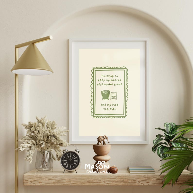 May include: A framed print with a light green background and a white border. The print features a green illustration of a cup of matcha and a matcha powder container. The text reads "Hustling to keep my matcha ceremonial grade and my vibe top-tier".