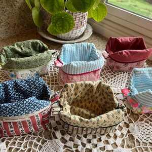 May include: A collection of six fabric baskets in various patterns and colors. The baskets feature floral, striped, and patterned designs in shades of blue, red, green, and yellow. Each basket has a contrasting interior lining.