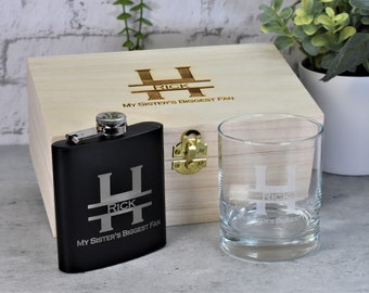 May include: A wooden box with a hinged lid, engraved with the text "H Rick My Sister's Biggest Fan". The box contains a black flask with the same engraving and a clear glass with the same engraving.