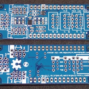 May include: Two blue MKR I2C Shield circuit boards with white markings and text. The boards have numerous holes and electronic components. Text includes "v1.8 MKR I2C SHIELD" and website URLs. The boards are designed for electronic projects.