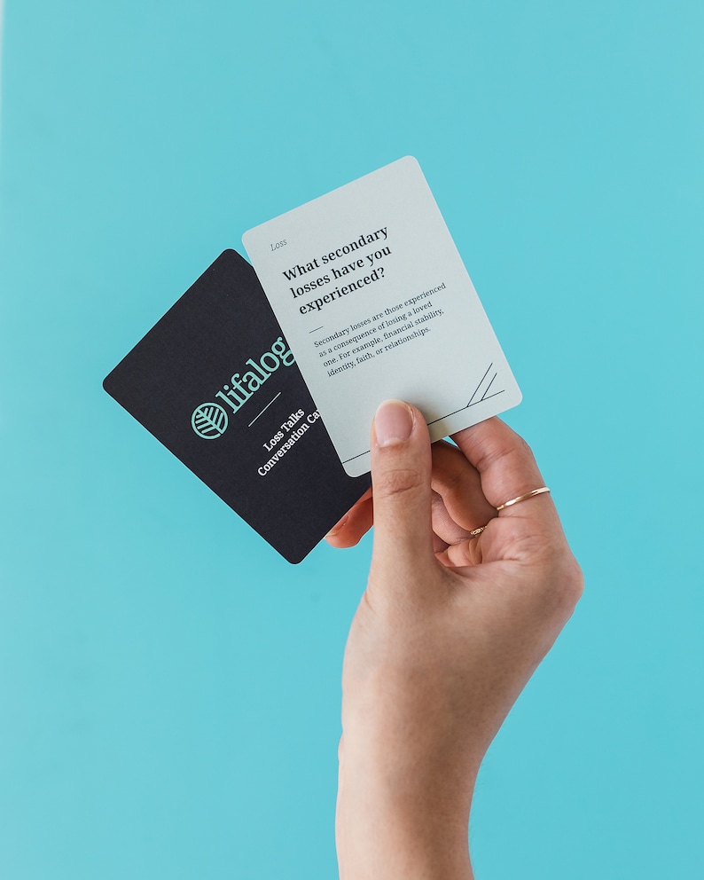 May include: A set of conversation cards with a teal leaf logo and the text "lifalog Loss Talks Conversation Cards". The card in the foreground is light gray with the text "Loss What secondary losses have you experienced? Secondary losses are those experienced as a consequence of losing a loved one. For example, financial stability, identity, faith, or relationships."